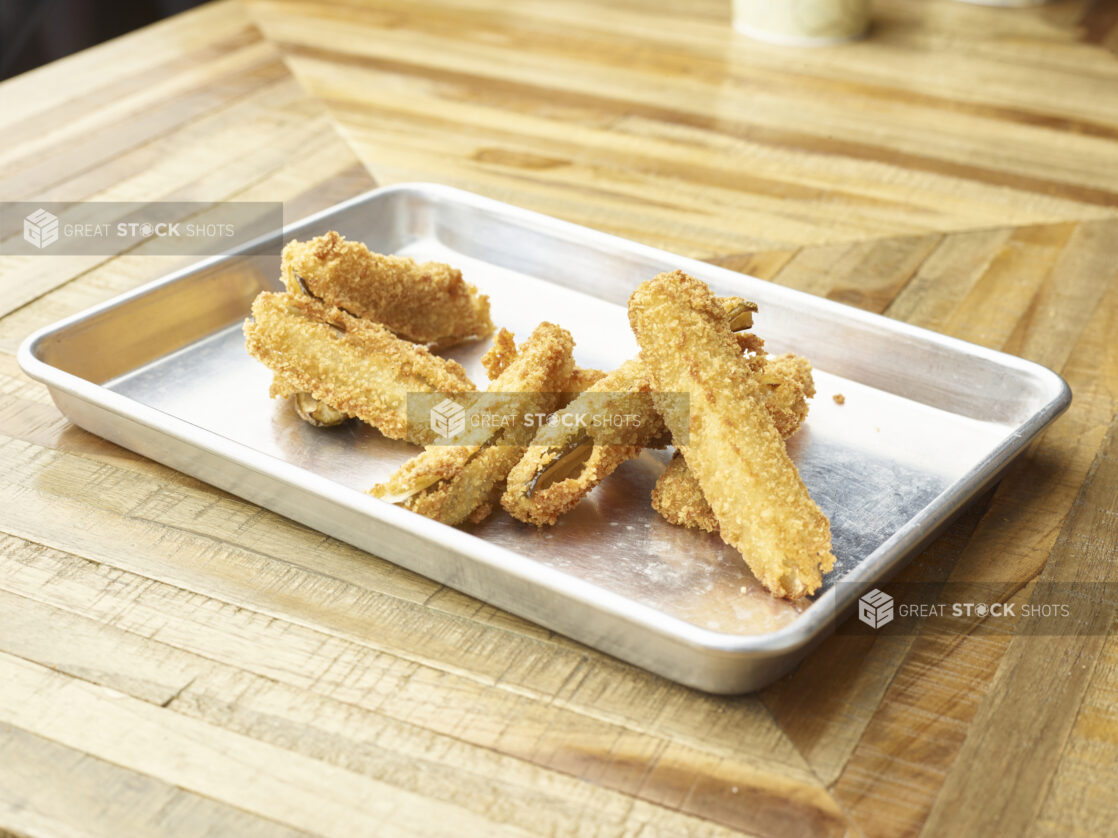 Close Up of Deep Fried Breaded Pickle Spears on a Stainless Steel Platter on a Parquet Wooden Table