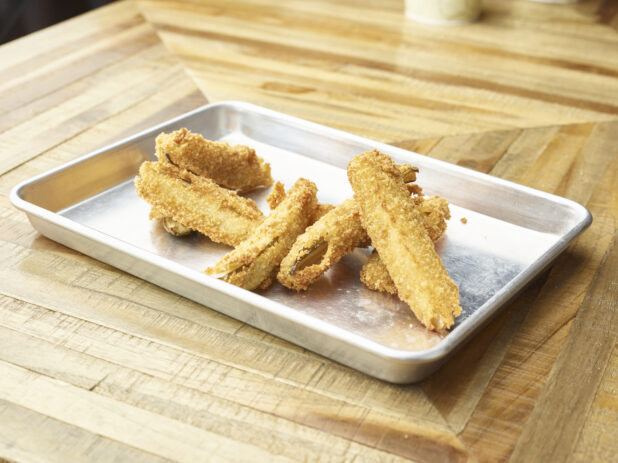Close Up of Deep Fried Breaded Pickle Spears on a Stainless Steel Platter on a Parquet Wooden Table