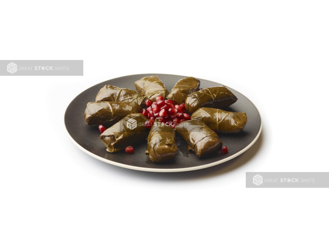 Stuffed Grapevine Leaves and Pomegranate Seeds on a Round Black Ceramic Dish, on a White Background for Isolation