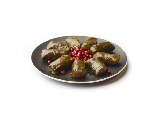 Stuffed Grapevine Leaves and Pomegranate Seeds on a Round Black Ceramic Dish, on a White Background for Isolation