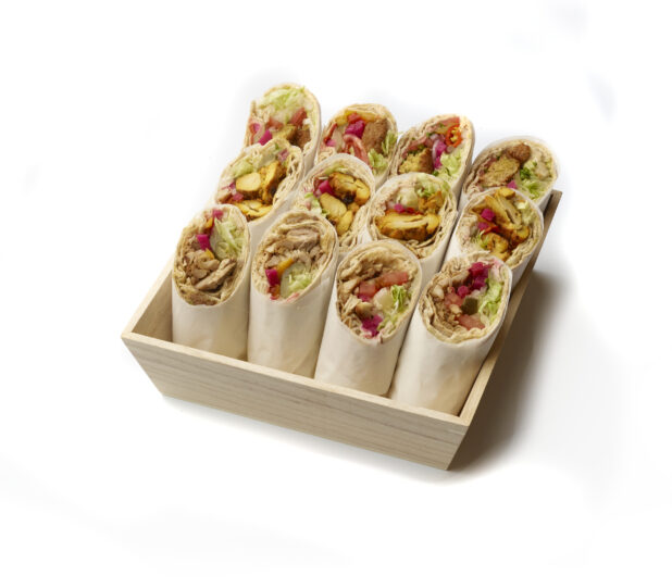 Deep Square Wood Serving Tray Filled with Chicken Shawarma, BBQ Chicken and Falafel Pita Wraps with Fresh Vegetable Toppings, Rolled in Parchment Paper on a White Background for Isolation