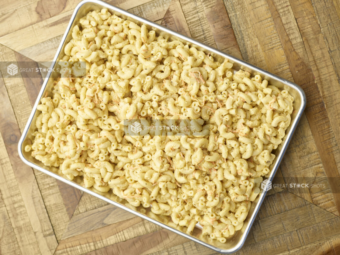 Overhead View of a Metal Baking Sheet Full of Prepared Macaroni Pasta Salad for Catering or a Party Tray, on a Wooden Parquet Table