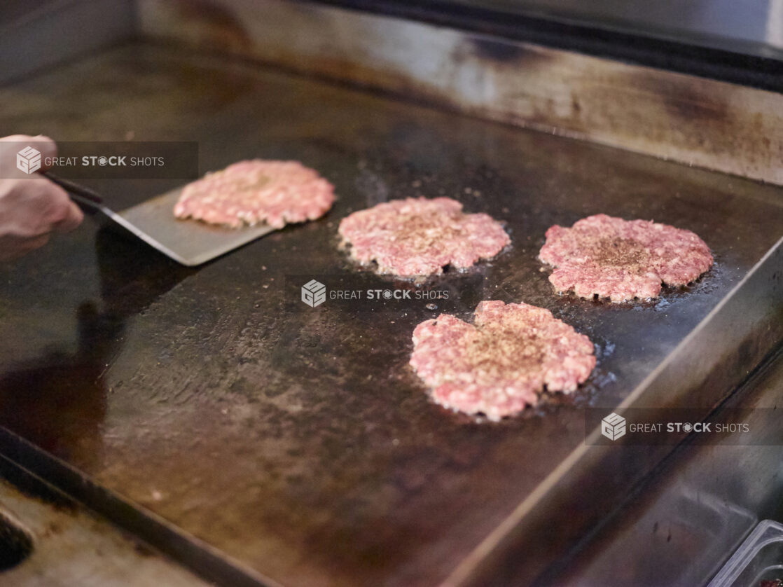 Smashed Beef Burger Patties Sizzling on a Flat Top Grill as a Chef Flips Them, in a Kitchen of a Gourmet Burger Restaurant