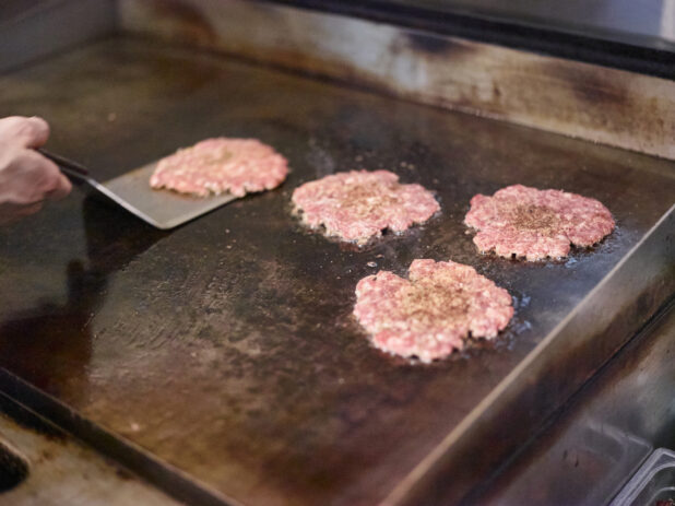 Smashed Beef Burger Patties Sizzling on a Flat Top Grill as a Chef Flips Them, in a Kitchen of a Gourmet Burger Restaurant