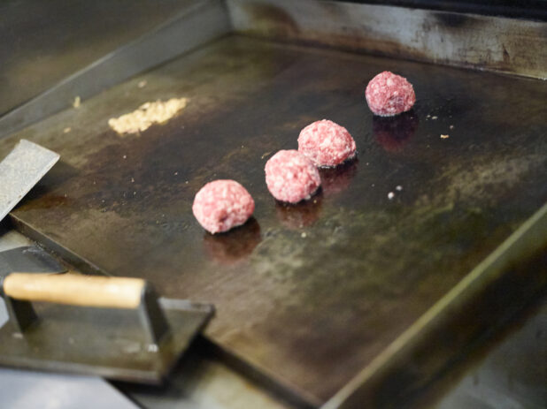 Ground Beef Meatballs Being Prepared to be Pressed on a Flat Top Grill to Cook Smash Burgers in a Gourmet Burger Restaurant