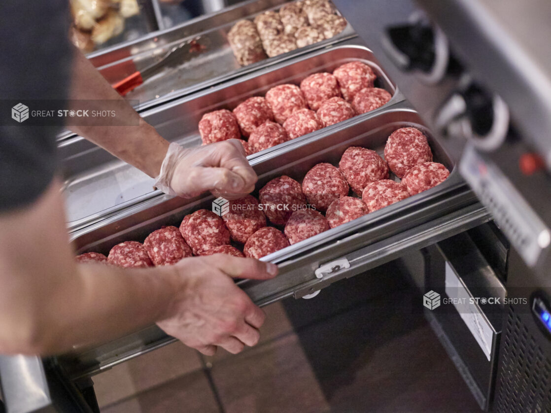 Chef's Hands Preparing Trays of Ground Beef Burger Patties Shaped into Balls for Grilling, in a Kitchen of a Gourmet Burger Restaurant