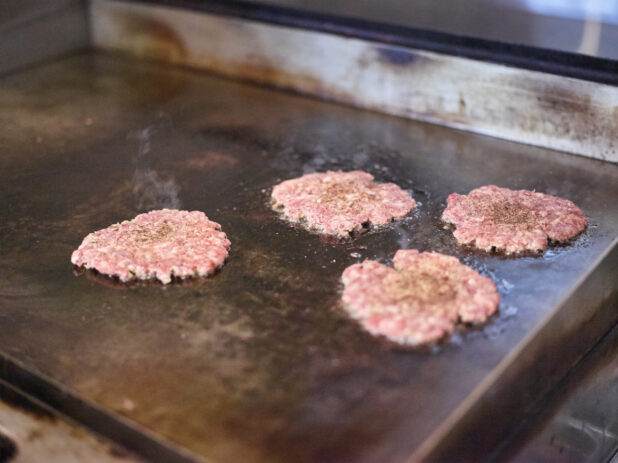 Smashed Beef Burger Patties Sizzling on a Flat Top Grill, in the Kitchen of a Gourmet Burger Restaurant