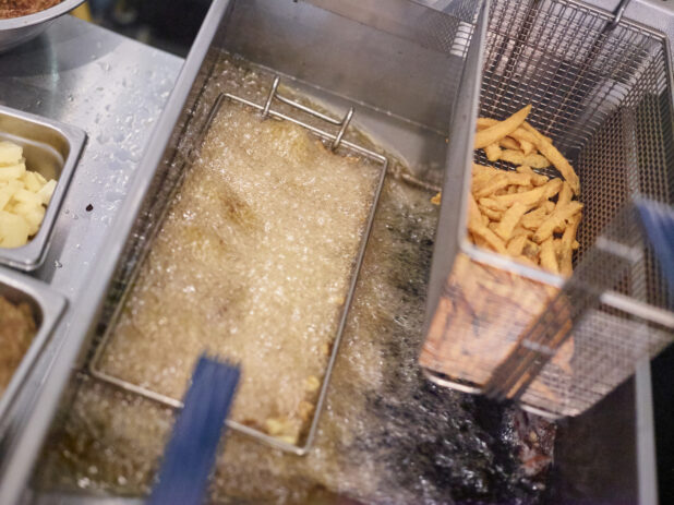 Close Up of a Commercial Kitchen Fryer with French Fries Being Cooked in Hot Oil in the Kitchen of a Gourmet Burger Restaurant