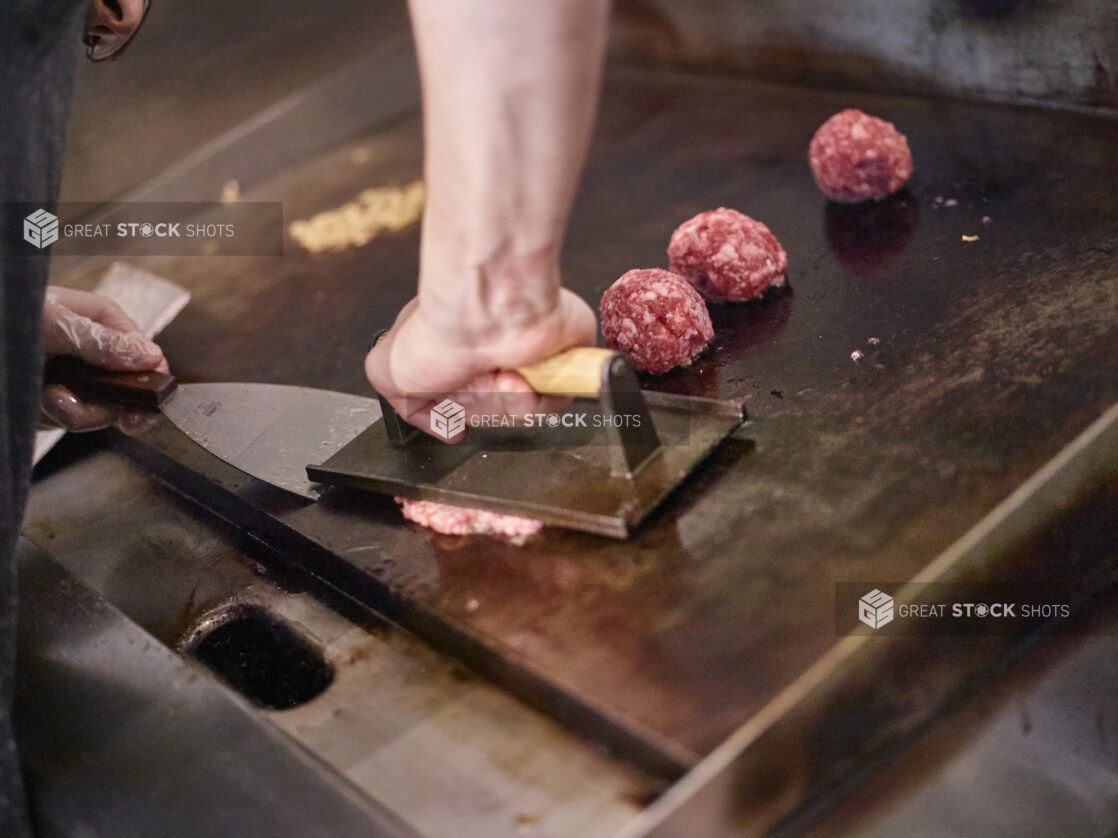 Chef Hands Pressing Ground Beef Meatballs on a Flat Top Grill to Cook Smash Burgers in a Gourmet Burger Restaurant