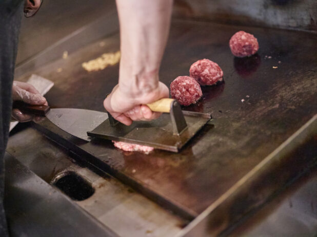 Chef Hands Pressing Ground Beef Meatballs on a Flat Top Grill to Cook Smash Burgers in a Gourmet Burger Restaurant