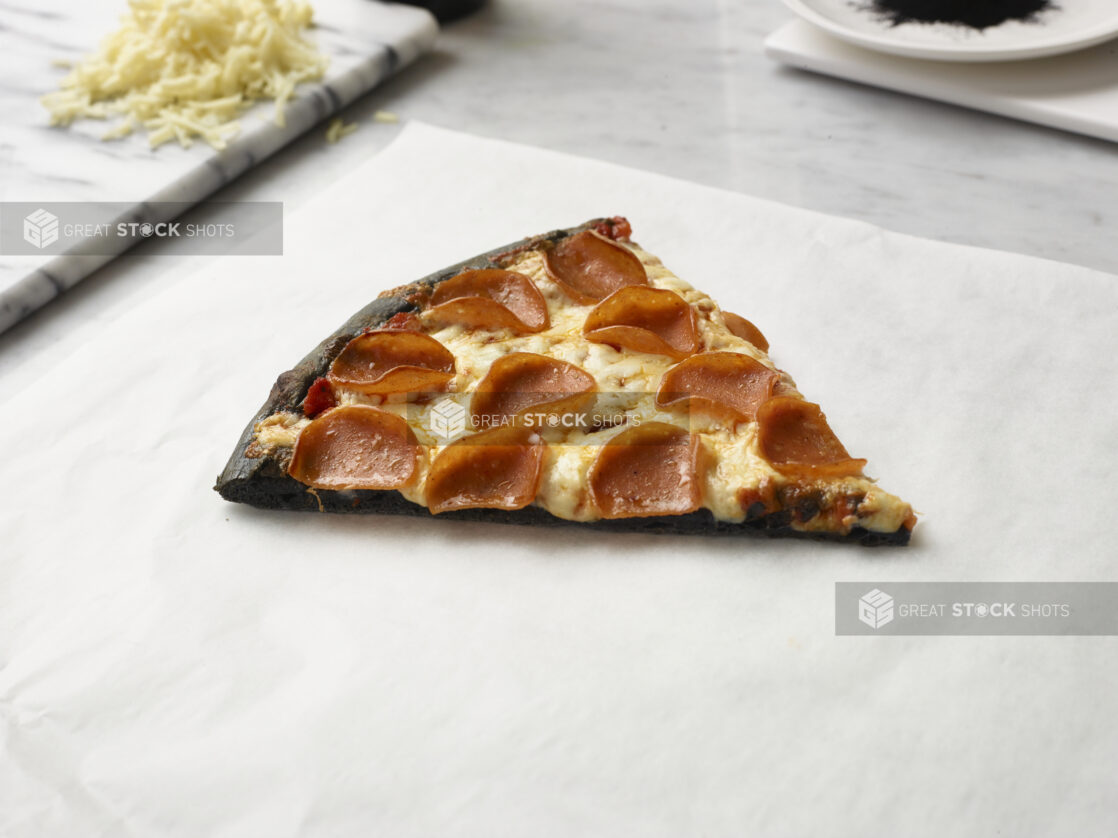 Slice of Pizza with a Charcoal Infused Pizza Crust, Pepperoni and Cheese Toppings on a Marble Counter Surface