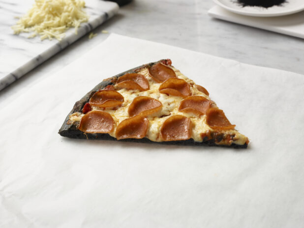 Slice of Pizza with a Charcoal Infused Pizza Crust, Pepperoni and Cheese Toppings on a Marble Counter Surface