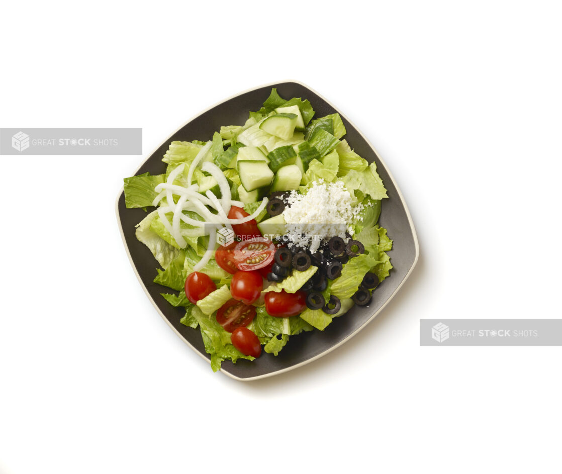 Overhead View of a Plain Greek Salad with Cherry Tomatoes, Cucumber, Black Olives, Feta and White Onions on a Square Black Ceramic Dish, on a White Background for Isolation