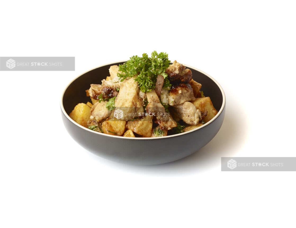 Garlic Potatoes and Chicken Shawarma Pieces Topped with Fresh Parsley Garnish in a Round Black Ceramic Bowl on a White Background for Isolation