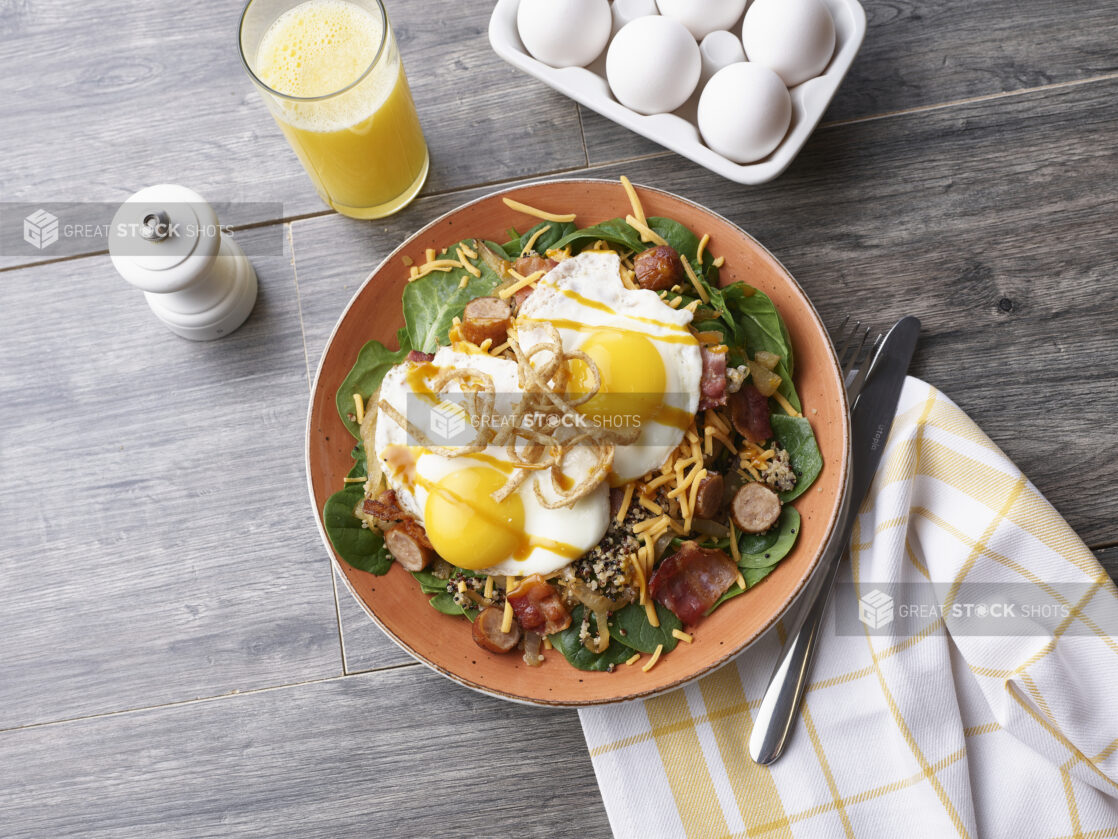 A breakfast spinach salad with eggs over easy in a ceramic bowl on a grey wood tabletop