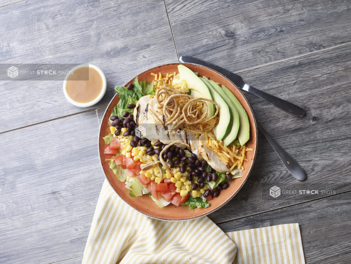 A Cobb style salad with black bean and corn in a coral ceramic bowl on a wood background