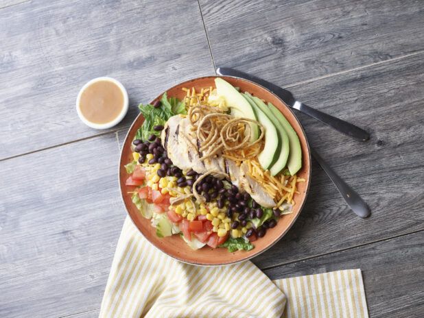 A Cobb style salad with black bean and corn in a coral ceramic bowl on a wood background