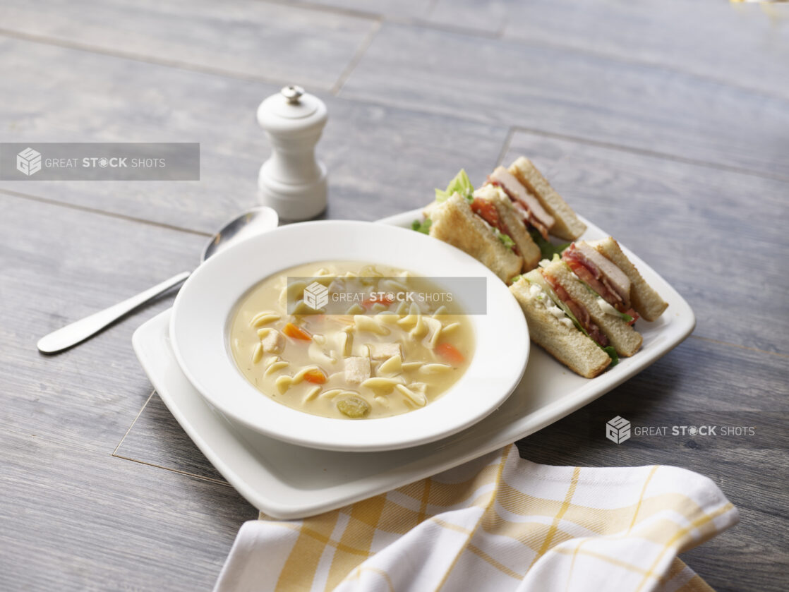 Chicken noodle soup with a half clubhouse sandwich on a grey wood tabletop