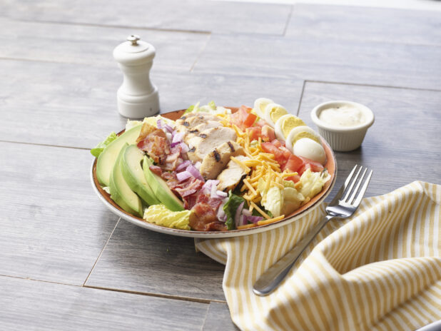 A Cobb salad in a ceramic Bowl on a wood background