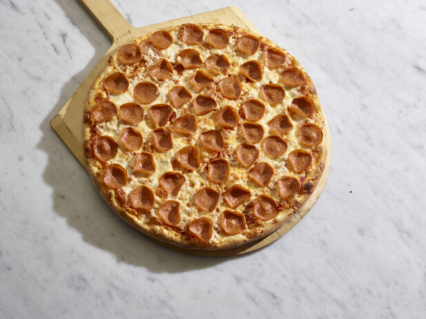 A traditional style pepperoni pizza on a wooden pizza peel on a marble background