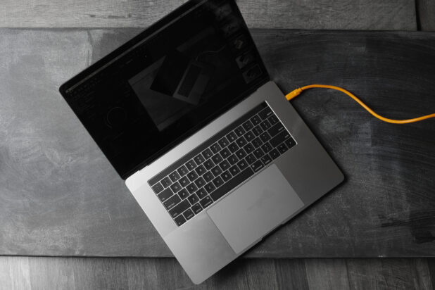 Overhead View of an Open MacBook Laptop with a Blank Screen and an Orange Cable, on a Black Slate Surface in an Indoor Setting