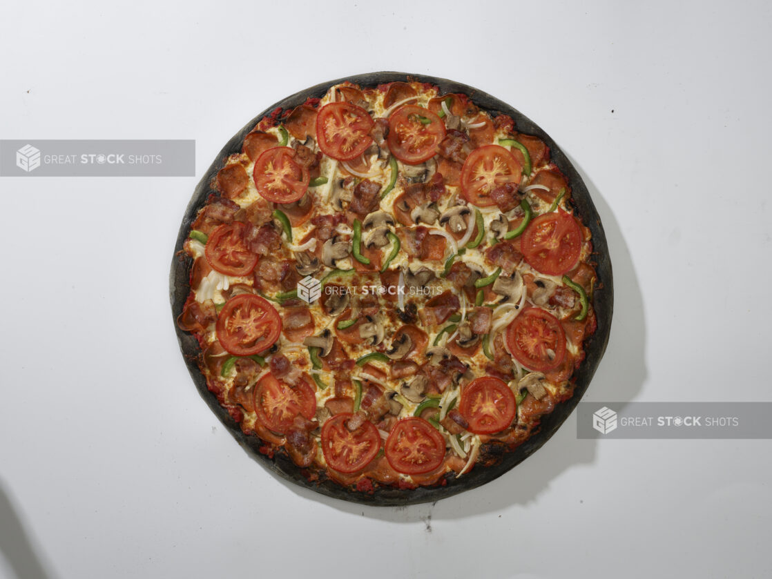 Overhead View of a Whole Charcoal-Infused Super Deluxe Pizza with Pepperoni, Green Peppers, Mushrooms, Bacon, White Onions and Sliced Tomato Toppings, on a White Background for Isolation