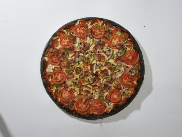 Overhead View of a Whole Charcoal-Infused Super Deluxe Pizza with Pepperoni, Green Peppers, Mushrooms, Bacon, White Onions and Sliced Tomato Toppings, on a White Background for Isolation