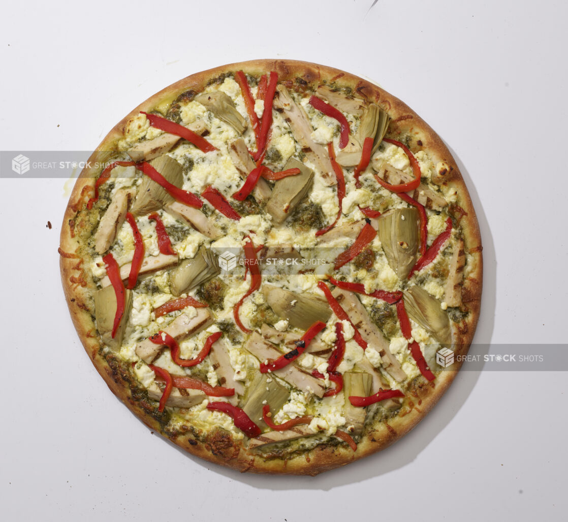 Overhead View of a Whole Specialty Pizza with Pesto Sauce, Sliced Artichoke Hearts, Roasted Red Peppers, Feta Cheese and Grilled Chicken Toppings, on a White Background for Isolation