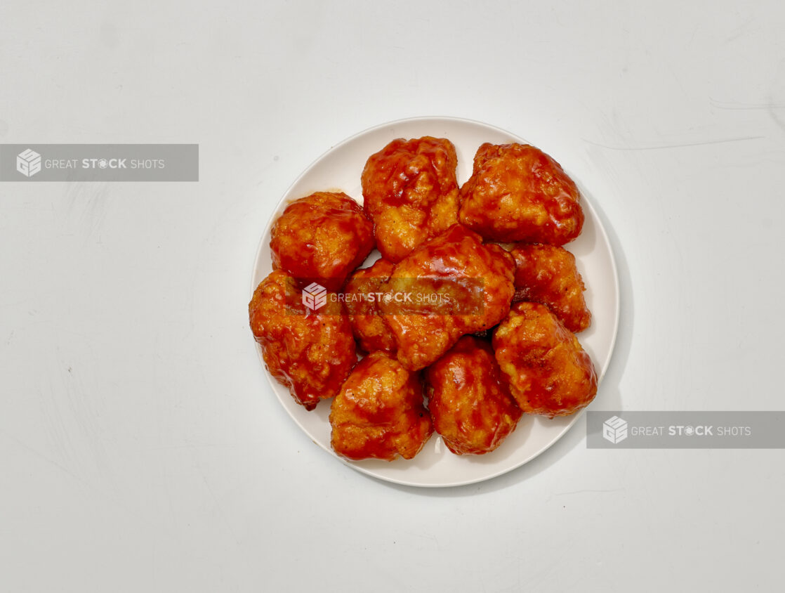 Overhead View of Sauced and Breaded Boneless Chicken Wings on a Round White Ceramic Dish, on a White Background for Isolation