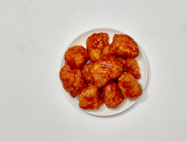 Overhead View of Sauced and Breaded Boneless Chicken Wings on a Round White Ceramic Dish, on a White Background for Isolation