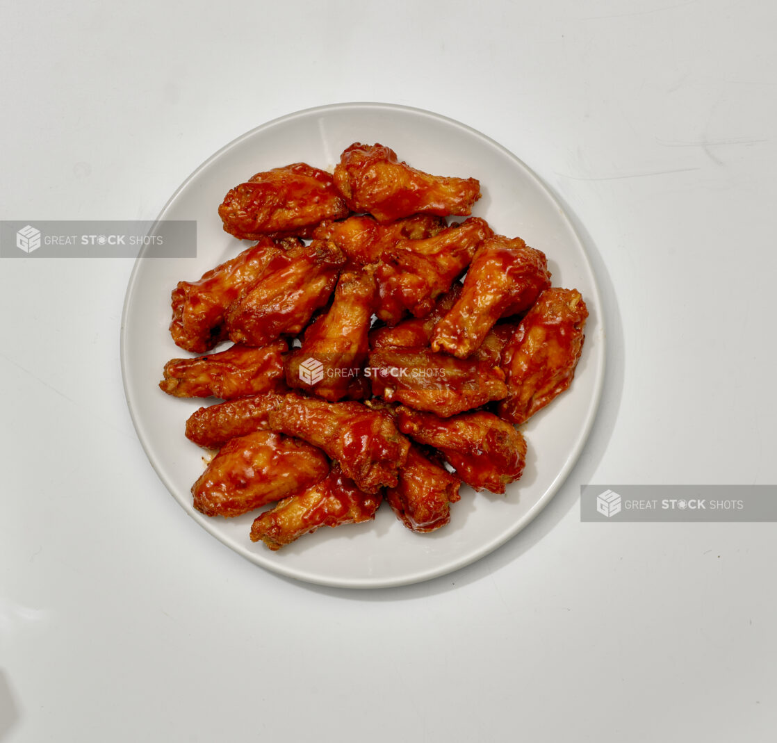 Overhead View of a Large Order of Sauced Chicken Wings on a Round White Ceramic Dish, on a White Background for Isolation