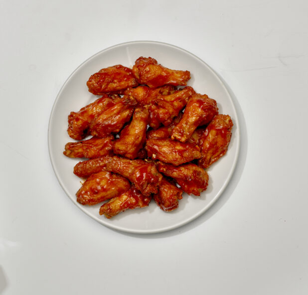 Overhead View of a Large Order of Sauced Chicken Wings on a Round White Ceramic Dish, on a White Background for Isolation