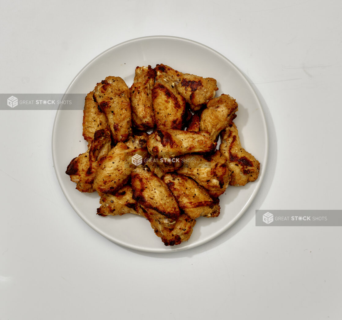 Overhead View of a Large Order of Roasted Italian Herb Chicken Wings on a Round White Ceramic Dish, on a White Background for Isolation