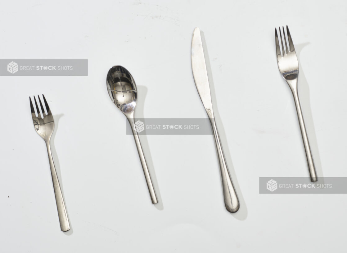 Overhead View of Stainless Steel Cutlery: Butter Knife, Forks and Spoon, on a White Background for Isolation