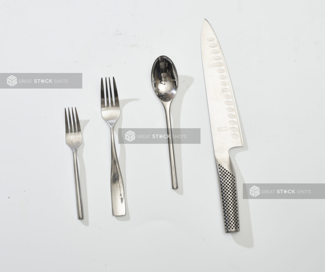 Overhead View of Stainless Steel Cutlery and an Engineered Steel Kitchen Knife, on a White Background for Isolation