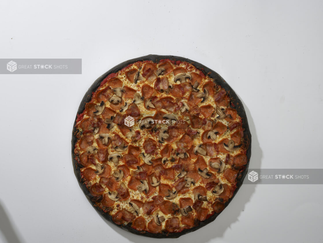 Overhead View of a Whole Charcoal-Infused Canadian Pizza with Pepperoni, Bacon and White Mushrooms Toppings, on a White Background for Isolation