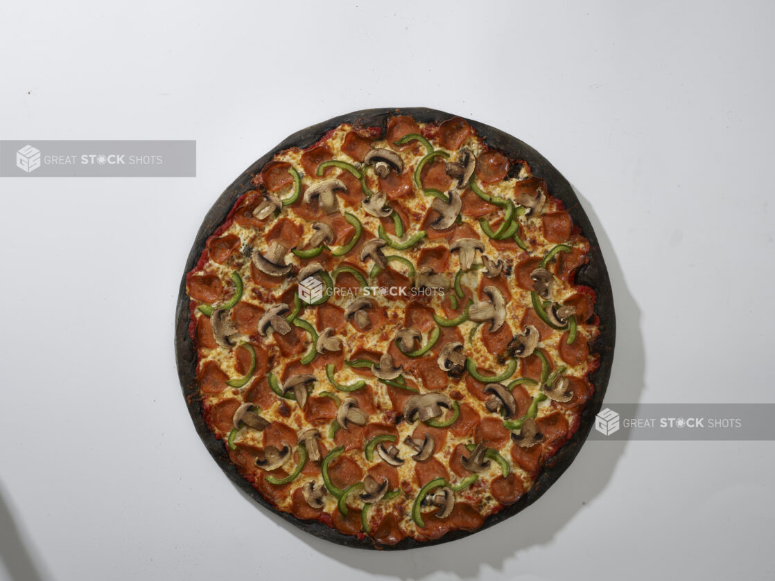 Overhead View of a Whole Charcoal-Infused Pizza with Pepperoni, Green Peppers and Mushroom Toppings, on a White Background for Isolation