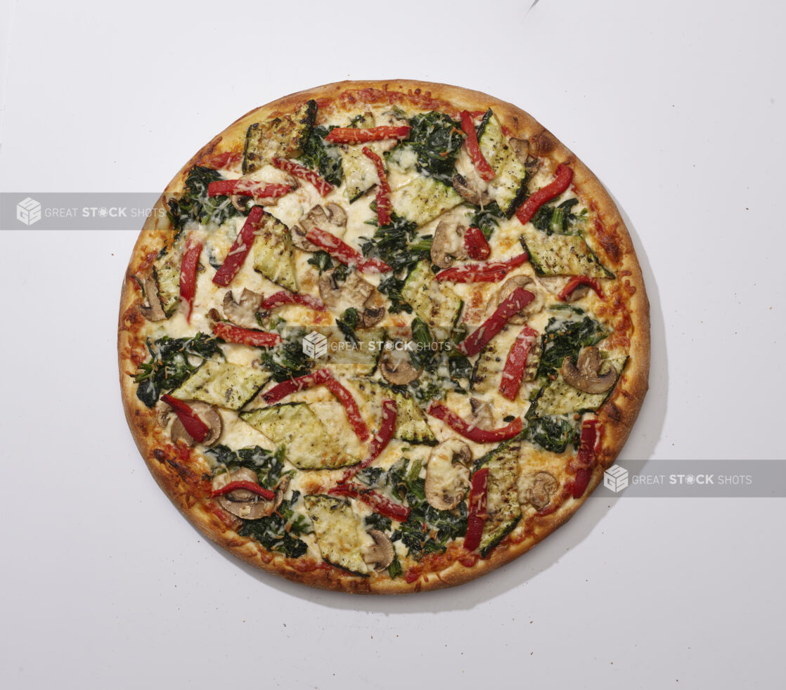 Overhead View of a Whole Specialty Pizza with Roasted Zucchini, White Mushrooms, Roasted Red Peppers, Sautéed Spinach and Parmigiana Cheese Toppings, on a White Background for Isolation