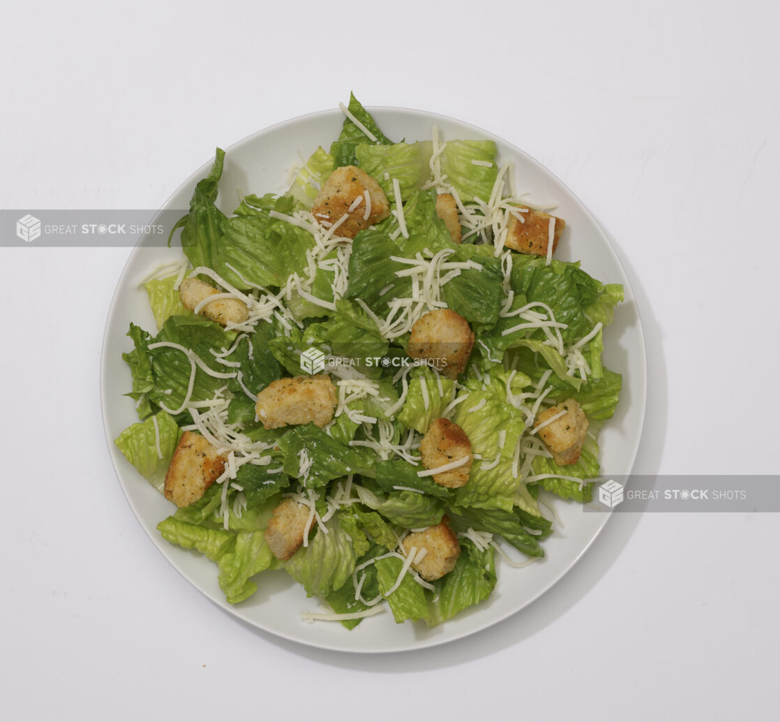 Overhead View of a Caesar Salad with Shredded Parmesan and Croutons on a Round White Ceramic Dish, on a White Background for Isolation