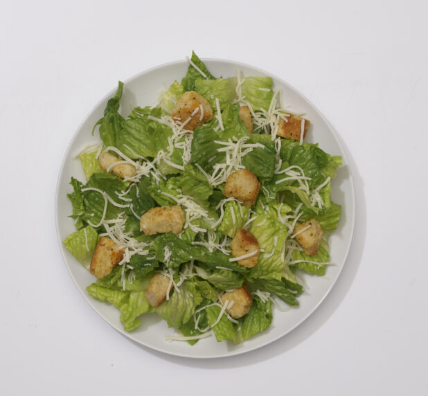 Overhead View of a Caesar Salad with Shredded Parmesan and Croutons on a Round White Ceramic Dish, on a White Background for Isolation