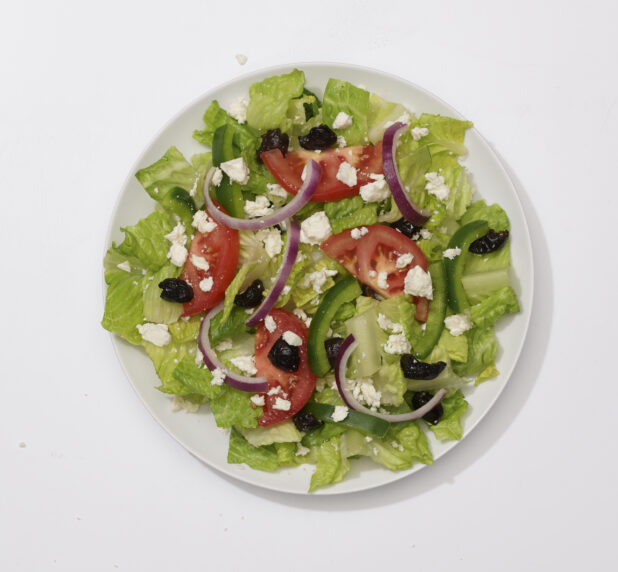 Overhead View of a Greek Salad with Sliced Tomatoes, Green Peppers, Red Onions, Black Olives and Feta Cheese on a Round White Ceramic Dish, on a White Background for Isolation