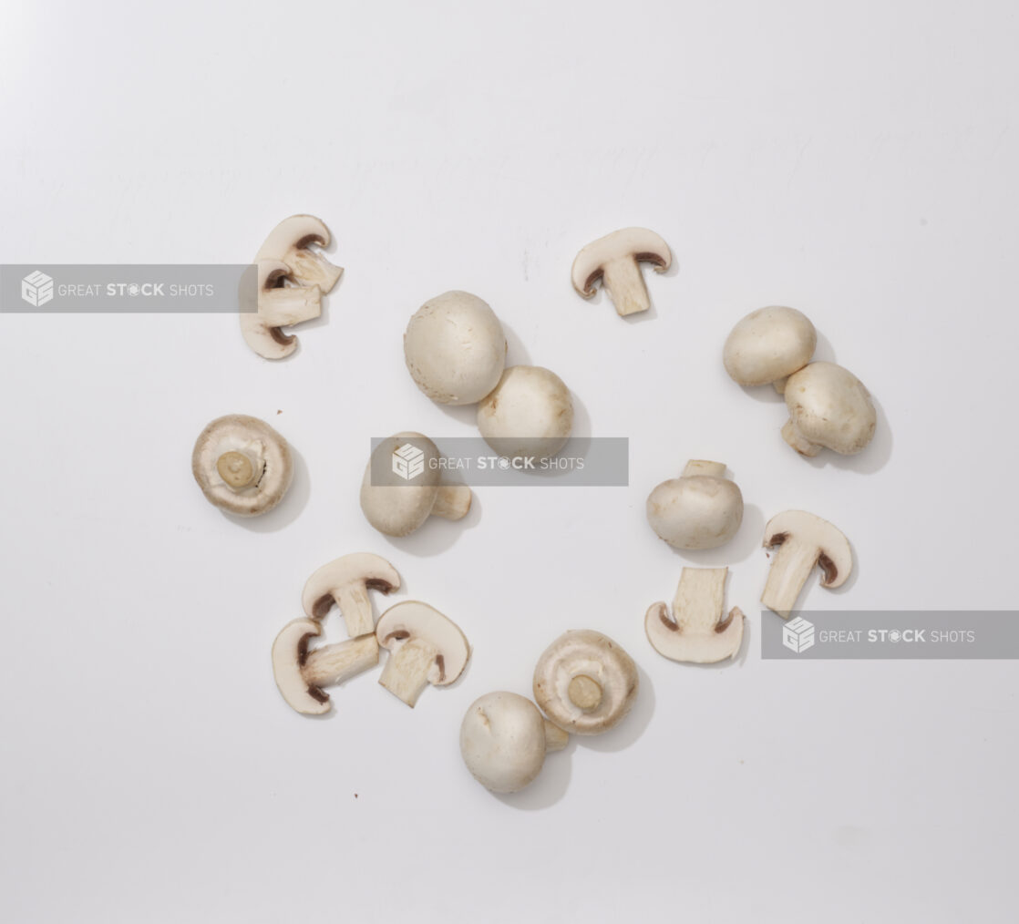 Overhead View of a Cluster of Whole and Sliced White Mushrooms, on a White Background for Isolation