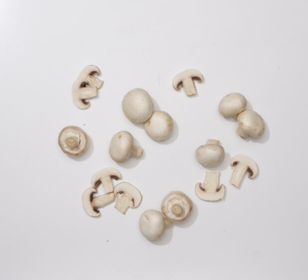 Overhead View of a Cluster of Whole and Sliced White Mushrooms, on a White Background for Isolation