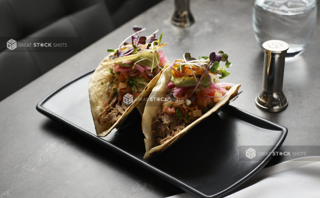 Pulled brisket tacos with pickled onions, pico de gallo, and avocado served with microgreen garnish on a black platter