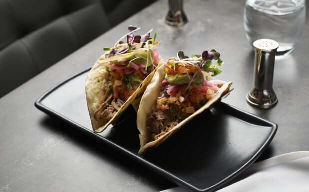 Pulled brisket tacos with pickled onions, pico de gallo, and avocado served with microgreen garnish on a black platter
