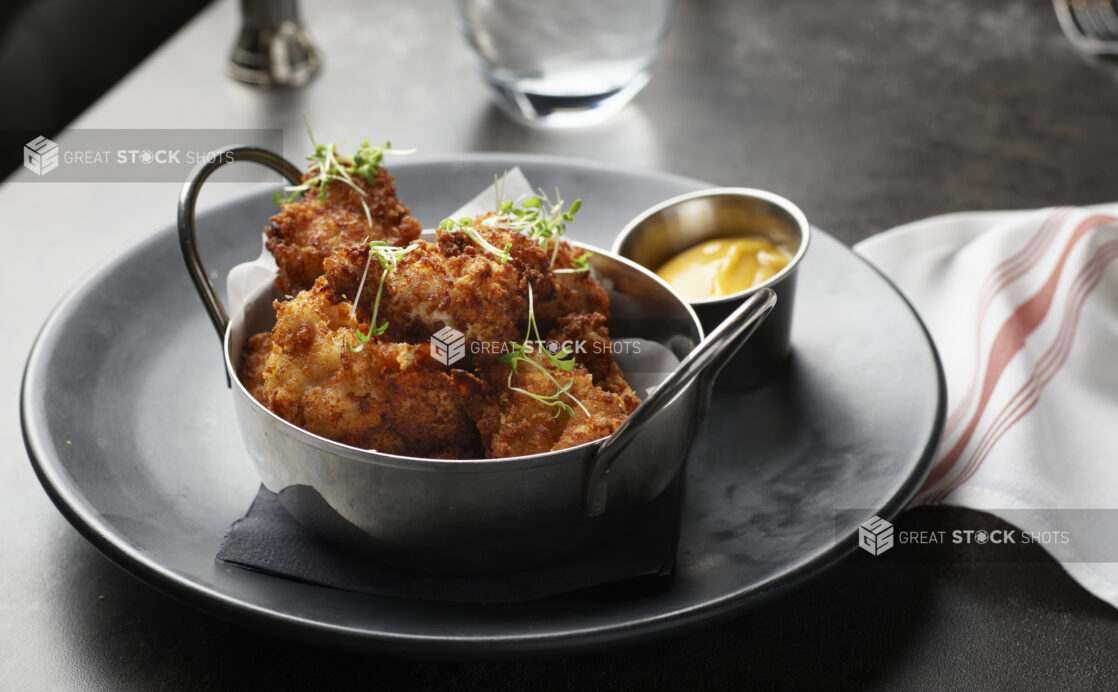 Crispy chicken bites with mustard-coloured dipping sauce on a dark plate