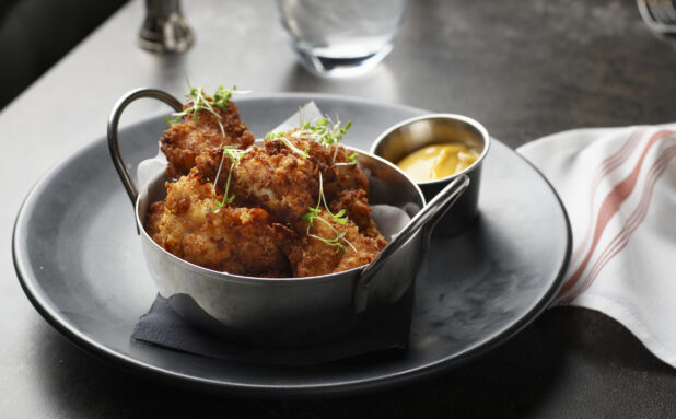 Crispy chicken bites with mustard-coloured dipping sauce on a dark plate