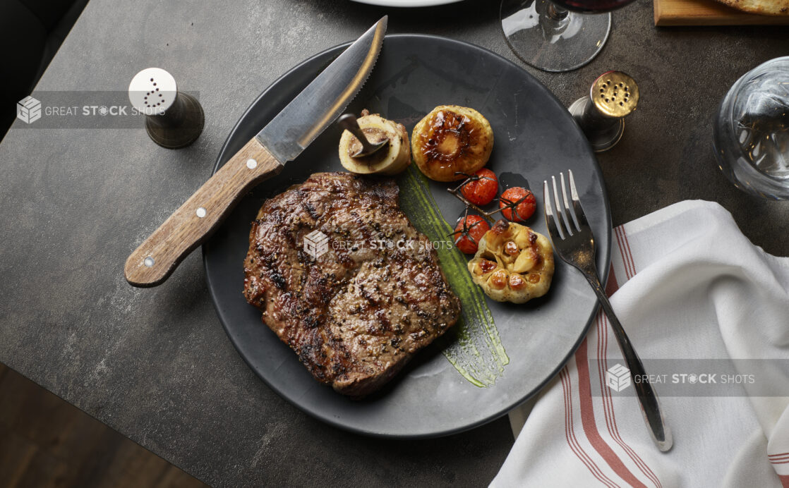 An overhead view of a steak dinner with bone marrow roasted garlic and mushroom and blistered cherry tomato