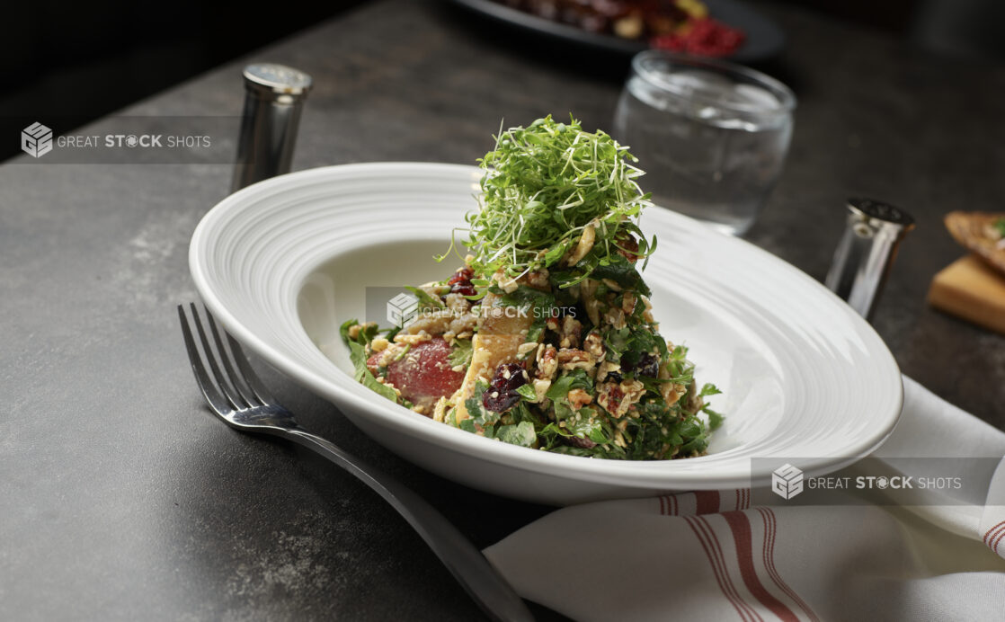 An herb and nut salad with microgreen garnish in a white bowl