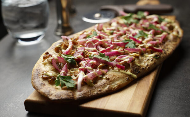 A flatbread appetizer with red onion, herbs and tahini